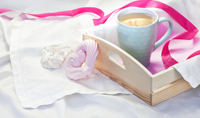 A tray with a cup of hot tea and homemade meringue in the form of heart in a bed on a white textile