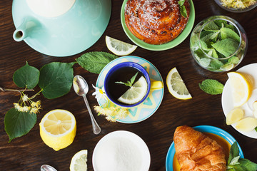 Cup of herbal tea with lemon and mint leaves, ginger root and croissant