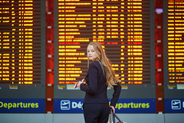 Woman with hand luggage in international airport terminal, looking at information board