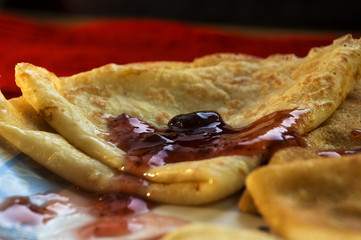 Pancakes with cherry jam and cutlery on a red background