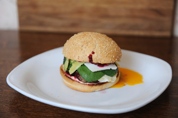 Burger with cutlet, vegetables, cheese and berry sauce closeup on a white plate on a wooden background