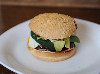 Burger with cutlet, vegetables, cheese and berry sauce closeup on a white plate on a wooden background