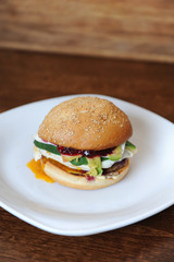 Burger with cutlet, vegetables, cheese and berry sauce closeup on a white plate on a wooden background