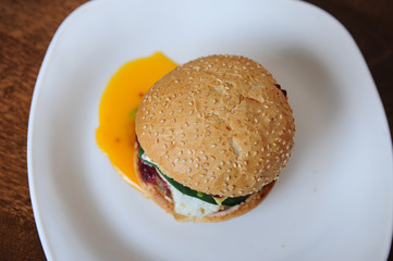 Burger with cutlet, vegetables, cheese and berry sauce closeup on a white plate on a wooden background