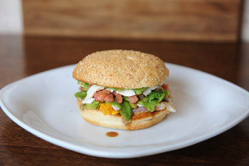 Burger with red fish, bacon, vegetables, cheese and berry sauce closeup on a white plate on a wooden background