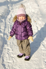 Child in lilac winter clothes standing in snow in park