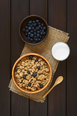 Dried berry and oatmeal breakfast cereal with fresh blueberries in wooden bowl with a glass of...