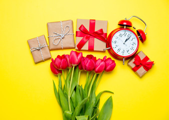 bunch of red tulips, alarm clock and beautiful gifts on the wonderful yellow background