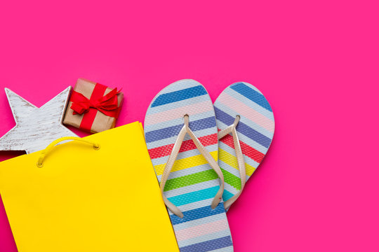 cute gift and star shaped toy in beautiful yellow shopping bag and colorful sandals on wonderful pink background