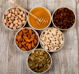 Pistachios, almonds, peanuts, pumpkin seeds, raisins and honey in ceramic plates.