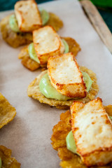 Cheese and avocado tostones, plantain crushed in small portions. In the top a fried cheese.