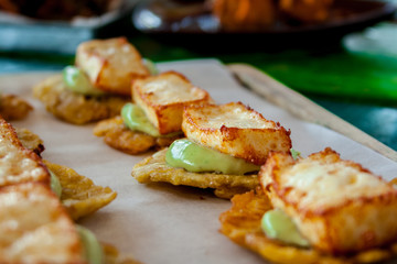 Cheese and avocado tostones, plantain crushed in small portions. In the top a fried cheese. - 138504569