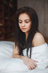 Sensual woman with dark hair sitting on a bed at home