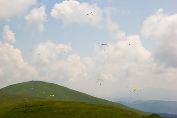 Paragliders fly among the clouds over green hills on a sunny day
