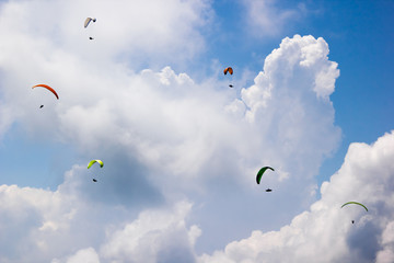 Paragliders fly among the white clouds on a sunny day
