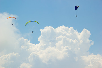 Paragliders fly among the white clouds on a sunny day