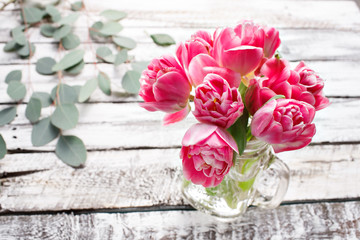 pink piony type tulips in tall glass jar on edge of white wooden rustic table. Spring melody mood of love