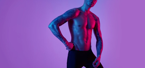 Fashion portrait of sport fit attractive man. Masculine naked torso tattooed hands. Color flash studio light.
