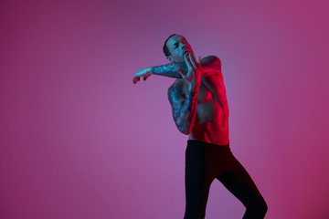 Fashion portrait of sport fit attractive man making arm stretch. Masculine naked torso, tattooed hands, hipster look. Color flash studio light