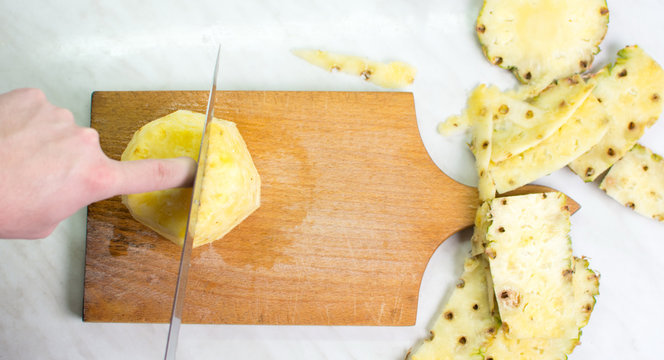 Male hands cutting  pineapple on a wooden board