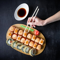 Traditional Japanese food. Top view. Flat lay. Sushi rolls and sauce and hand with chopsticks on a black background.