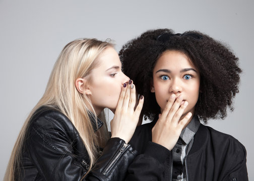 Two teenage hipster girls in studio. One says the other some terrible secret.