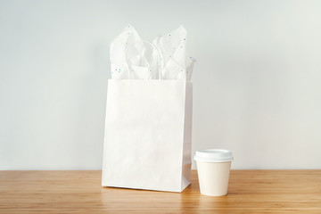 Mock-up of craft shopping bag and paper cup on the wooden table, Blank white package with handles and white cup with copy space for your design or logo