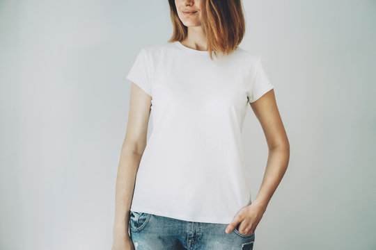 Young hipster girl wearing blue jeans and white blank t-shirt with space for your logo or design, mock-up of white cotton t-shirt, white wall in the background