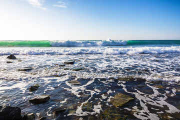 Ocean waves and stones on shore and blue sky