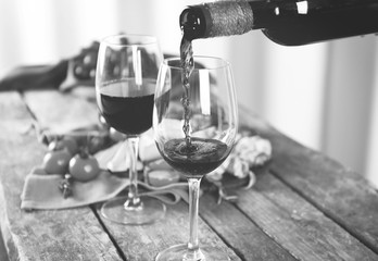 Pouring wine into glass on wooden table, toned in black and white