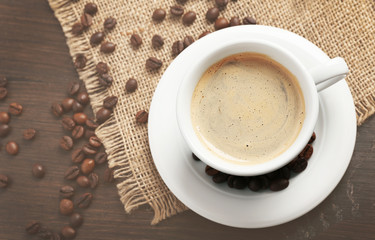 Aromatic cup of coffee with roasted beans on sackcloth