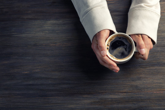 Male hands holding cup of coffee on wooden background