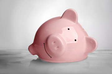 Pink piggy bank in water on light background