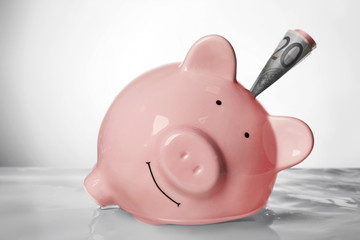 Pink piggy bank with banknote in water on light background