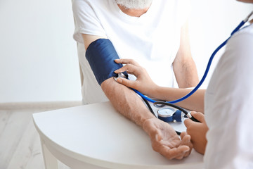 Nurse helping senior with measuring pressure on wooden table