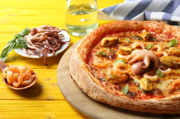 Gourmet seafood pizza and napkin on yellow wooden background