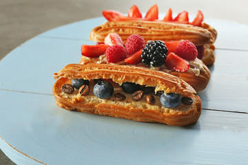 Delicious eclairs with berries on wooden tray