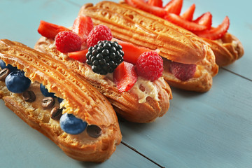 Delicious eclairs with berries on wooden tray