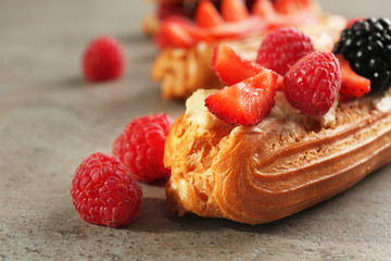 Delicious eclair with berries on light textured background