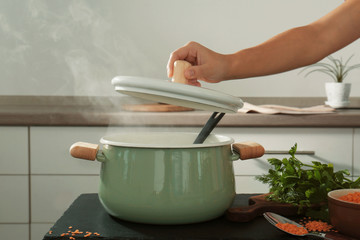 Female hand holding lid above enamelled pan in kitchen