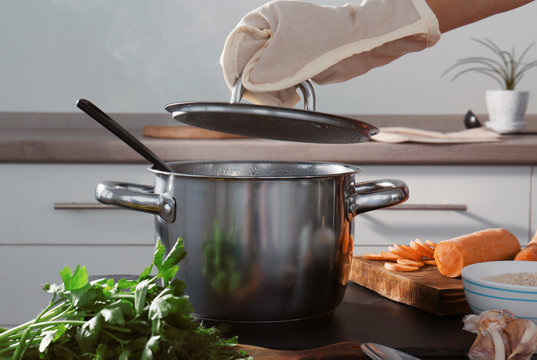 Woman Hand In Mitten Holding Lid Above Metal Pan In Kitchen