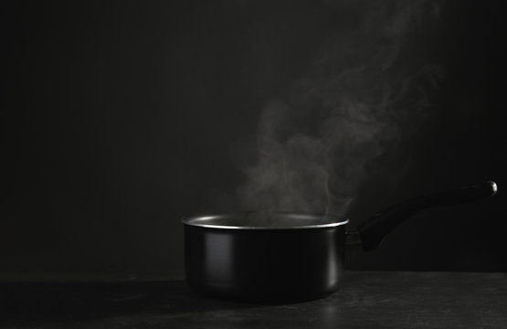 Saucepan with hot liquid on table against dark background