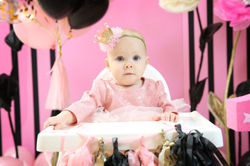 Fototapeta premium Cute little birthday girl sitting on high chair in room decorated for party