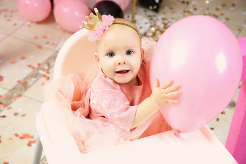 Obraz na płótnie Canvas Cute little birthday girl playing with balloon while sitting on high chair