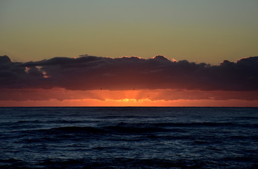 Beautiful sunrise cloudscape over ocean background. Sun rays beaming through picturesque clouds above sea. Blue sky with clouds, sea and sun on the horizon. Beautiful sunrise over the quiet calm sea.