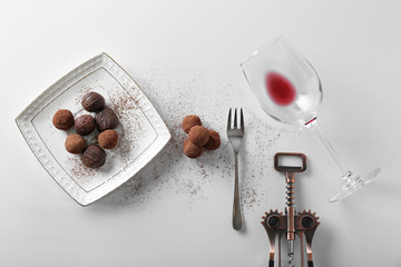 Delicious chocolate truffles and empty wine glass on white table
