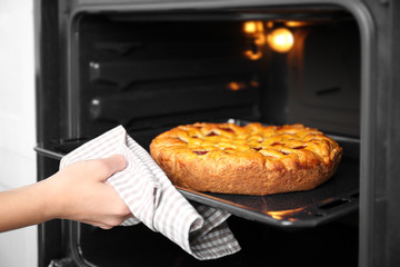 Woman hand taking baking tray with delicious pie from oven