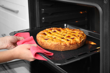 Woman hand taking baking tray with delicious pie from oven