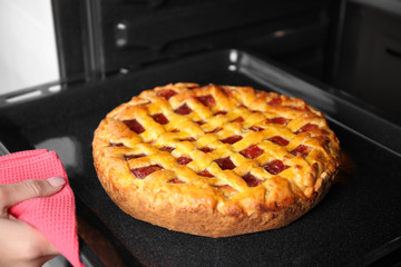 Woman hand taking baking tray with delicious pie from oven