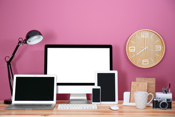 Computer display, laptop, tablet and smart phone on wooden table against color wall